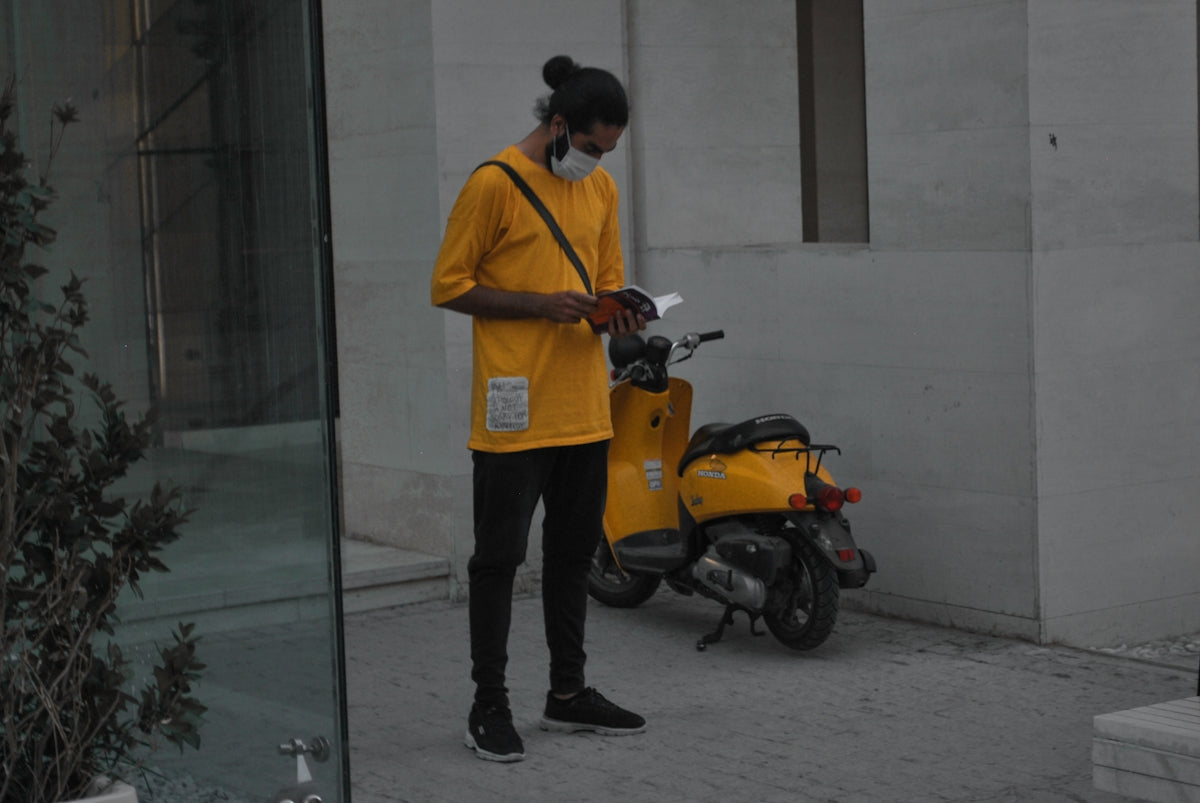 man in orange polo shirt and black pants standing beside orange motorcycle
