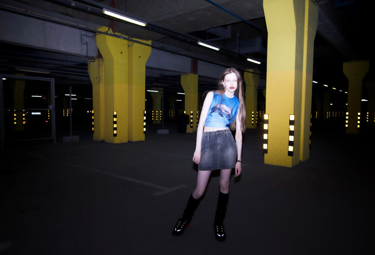 a woman in a blue shirt and black skirt standing in a parking garage