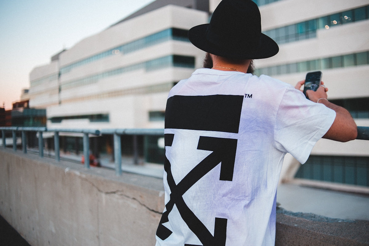 man in white and black t-shirt wearing black hat standing near white wall during daytime